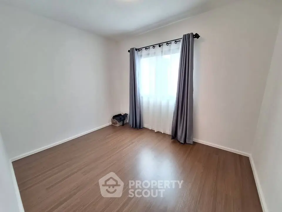 Spacious empty room with wooden flooring and large window with curtains, perfect for customization.
