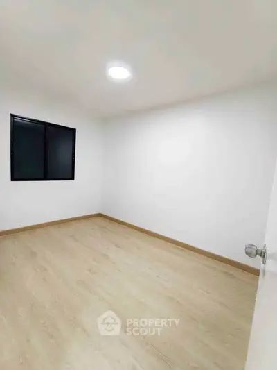Spacious empty bedroom with wooden flooring and modern window design.