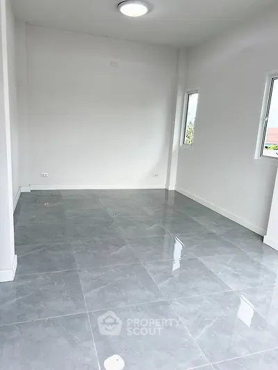 Spacious empty room with glossy tiled flooring and natural light.