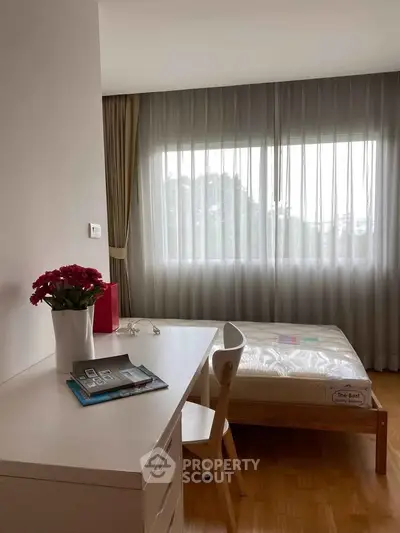 Bright bedroom with large window, wooden flooring, and modern furniture, perfect for cozy living.