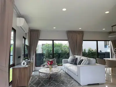 Spacious modern living room with elegant decor and large windows overlooking greenery.