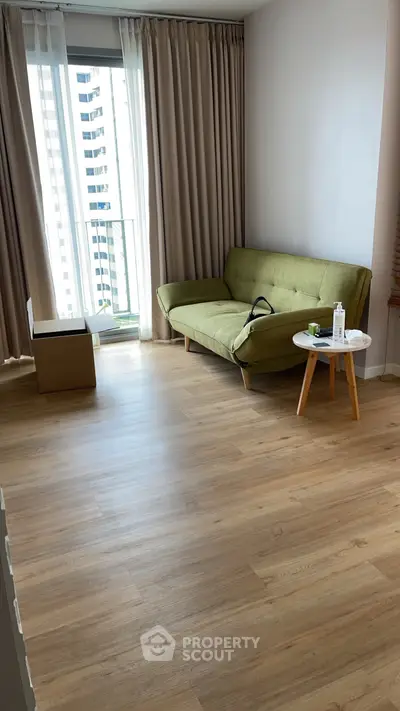 Modern living room with green sofa and wooden flooring, bright natural light from large window.