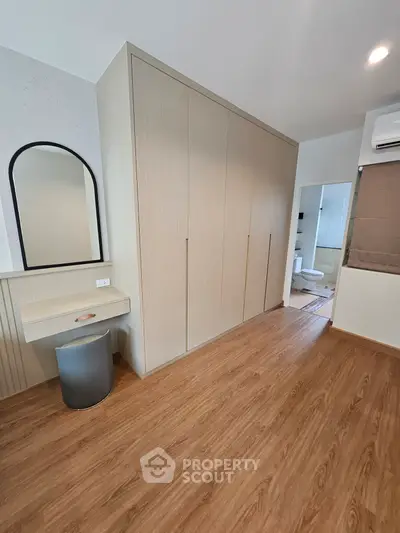 Modern bedroom with wooden flooring, built-in wardrobe, and a sleek vanity area.