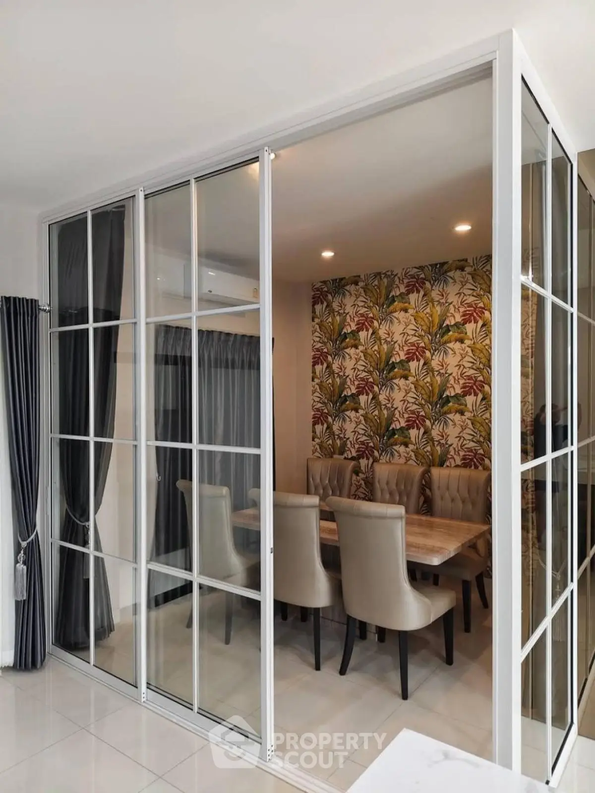 Elegant dining area with glass partition and floral wallpaper, featuring plush chairs and a stylish table.