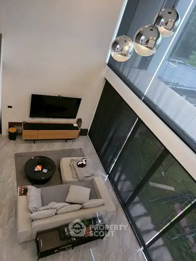 Modern living room with high ceiling and stylish decor, featuring large windows and contemporary lighting.