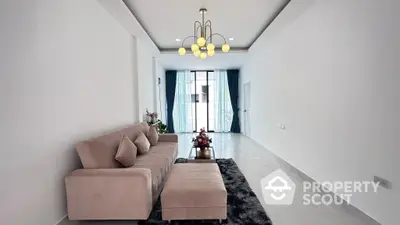 Spacious living room with modern minimalist decor, plush sofa set, elegant chandelier, and ample natural light from large windows leading to a balcony.