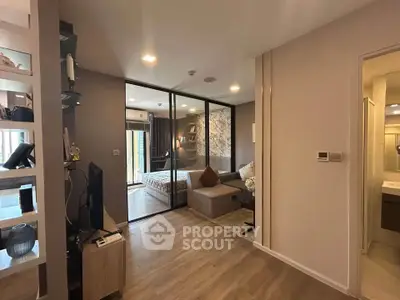 Modern open-plan living room with glass partition leading to a cozy bedroom, featuring stylish decor and wooden flooring.