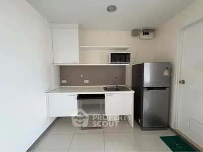 Modern kitchen with sleek white cabinets, microwave, and stainless steel fridge in a compact layout.