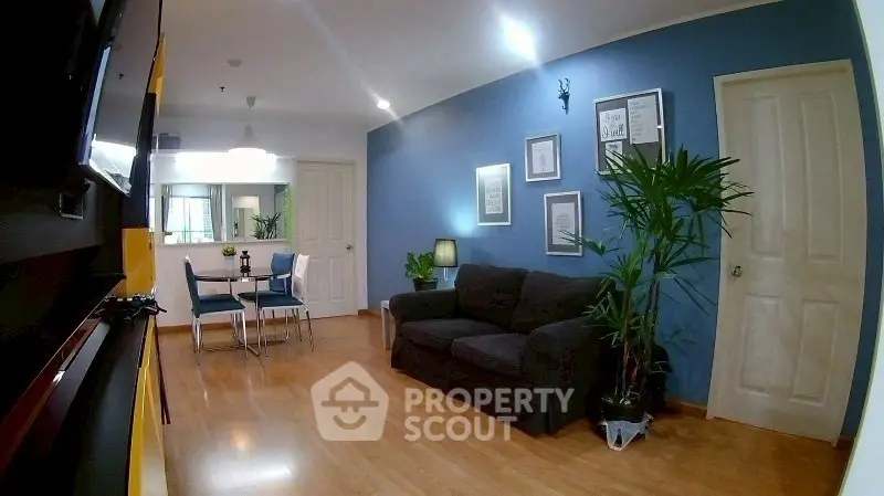 Modern living room with blue accent wall, cozy sofa, and dining area in open layout apartment.
