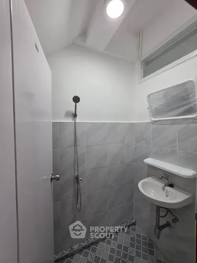 Modern minimalist bathroom with sleek shower and compact sink in a tiled setting.