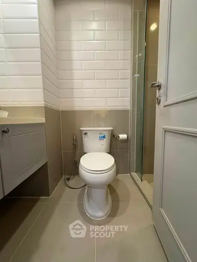 Modern bathroom with sleek design and neutral tones, featuring a toilet and shower area.