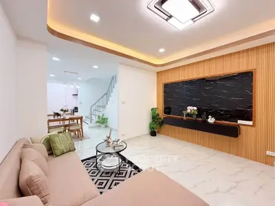 Modern living room with stylish decor and open dining area, featuring elegant lighting and sleek furniture.
