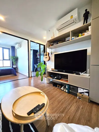Modern living room with stylish decor and open view into bedroom, featuring wooden flooring and sleek furniture.