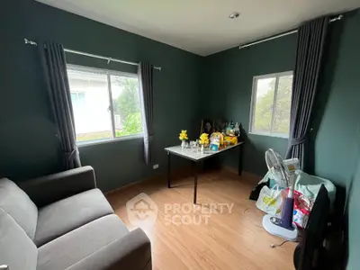 Cozy living room with dark green walls, wooden flooring, and ample natural light from two windows.