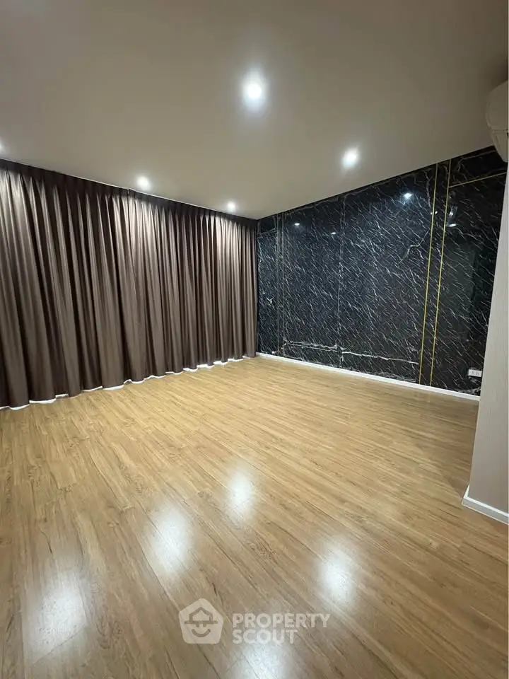Spacious empty room with wooden flooring and elegant dark curtains, perfect for customization.