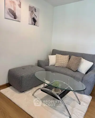 Cozy living room with modern gray sofa and glass coffee table on plush rug.