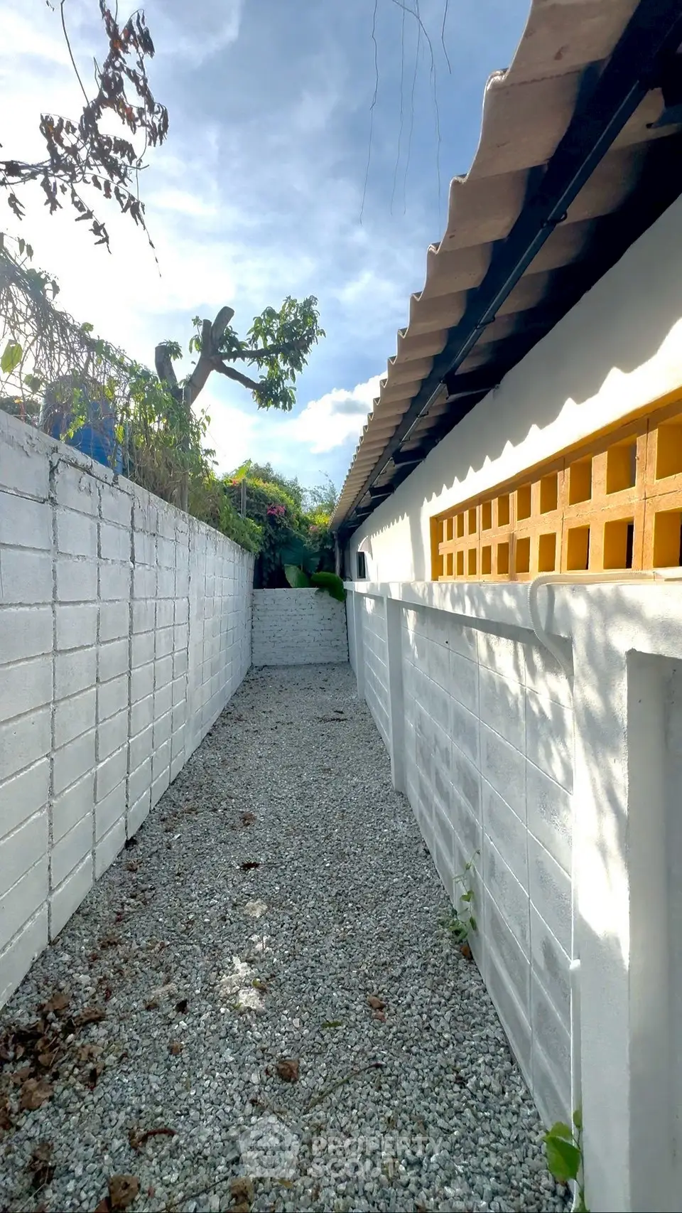 Charming exterior pathway with white brick walls and lush greenery, perfect for serene outdoor living.