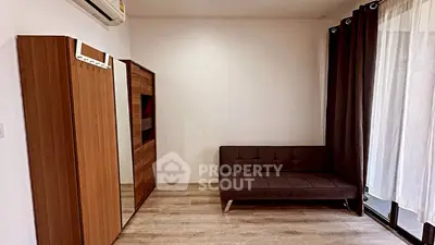 Modern living room with sleek sofa and wooden wardrobe, featuring elegant curtains and air conditioning.