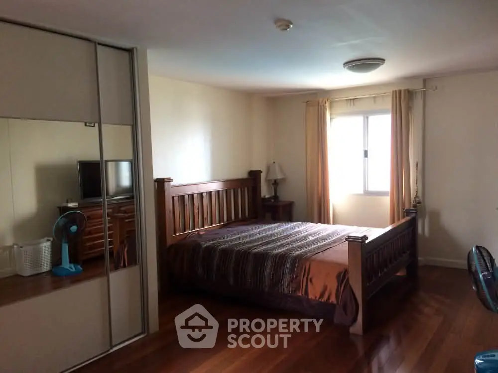 Spacious bedroom with wooden flooring and large window for natural light.