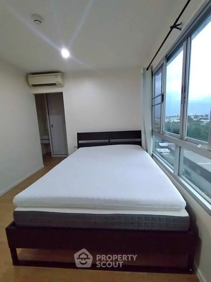 Spacious bedroom with large window offering city view and natural light.