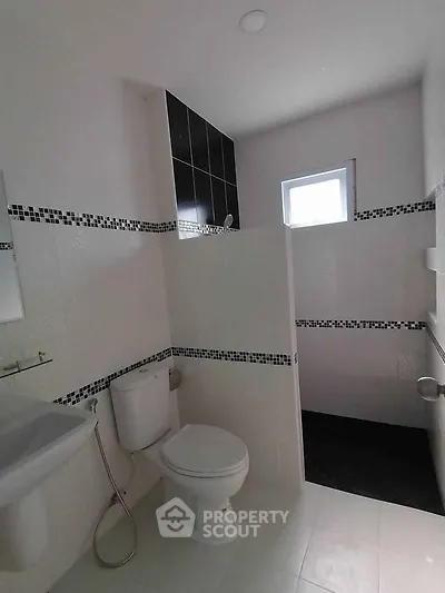 Modern bathroom with sleek black and white tiles, featuring a toilet and shower area.