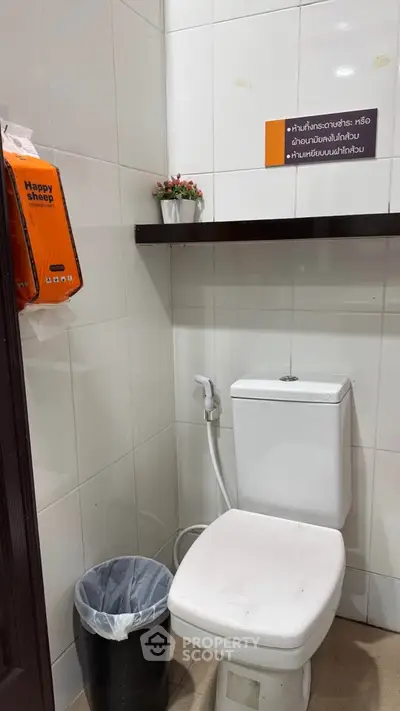 Compact bathroom with toilet, bidet, and wall shelf in a tiled setting.