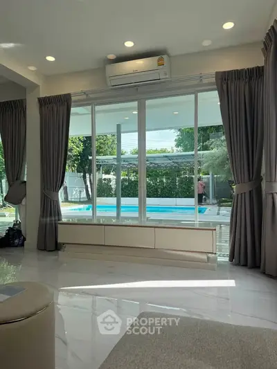 Spacious living room with pool view and large windows, perfect for relaxation.