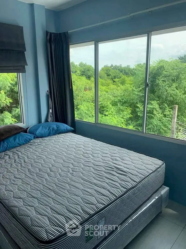 Cozy bedroom with large windows offering lush green views, perfect for relaxation.
