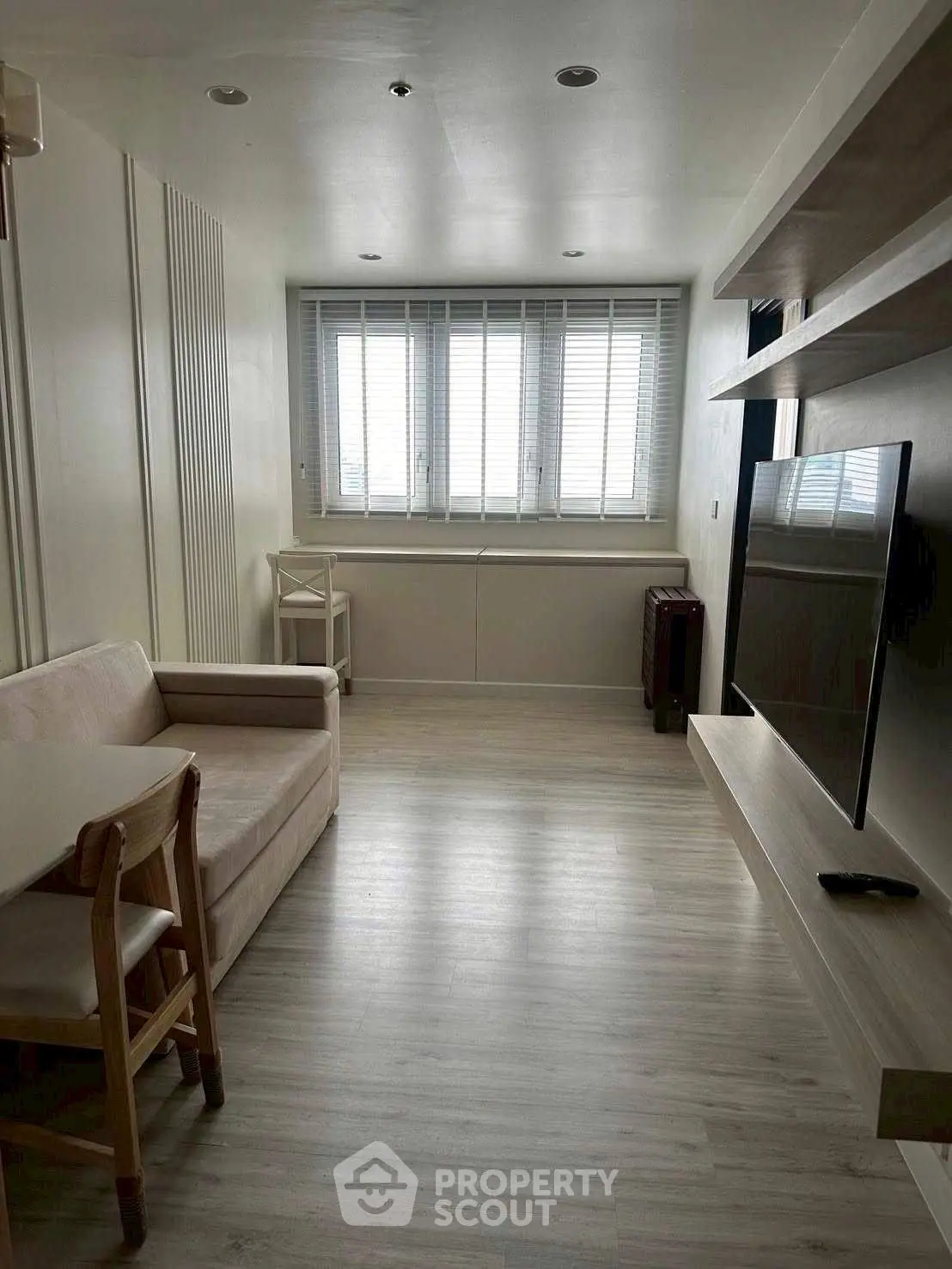 Modern living room with sleek design, featuring a cozy sofa, wall-mounted TV, and large window for natural light.