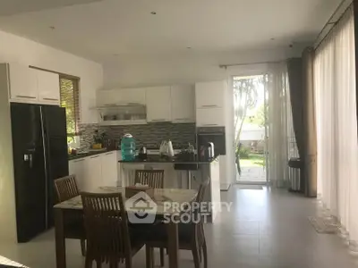 Modern kitchen with open layout and dining area, featuring sleek appliances and large windows.