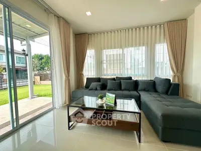 Spacious living room with modern sofa and glass coffee table, overlooking a lush garden through large windows.
