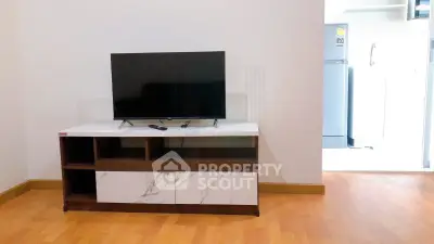 Modern living room with sleek TV stand and adjacent kitchen area featuring a refrigerator.