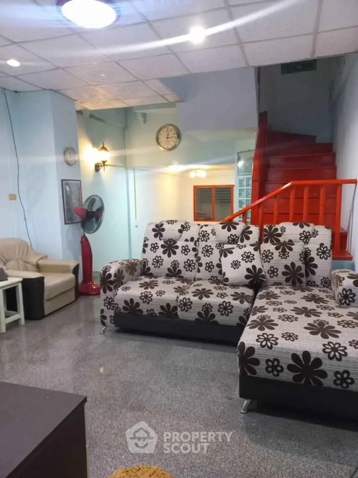 Spacious living room with floral sofa and red staircase, ideal for family gatherings.