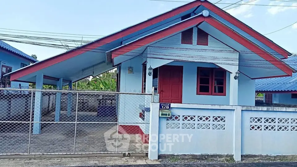 Charming blue house with red accents and gated driveway in a serene neighborhood.