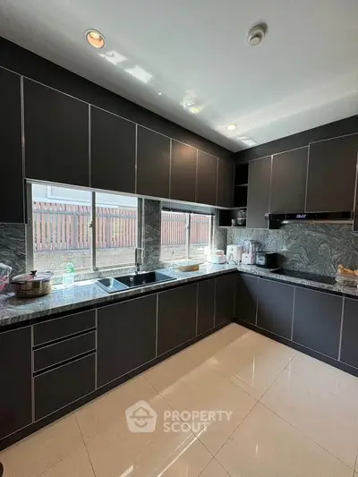 Modern kitchen with sleek dark cabinetry and marble countertops, featuring large windows for natural light.