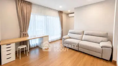 Spacious living room with modern sofa and study desk, featuring elegant curtains and wooden flooring.