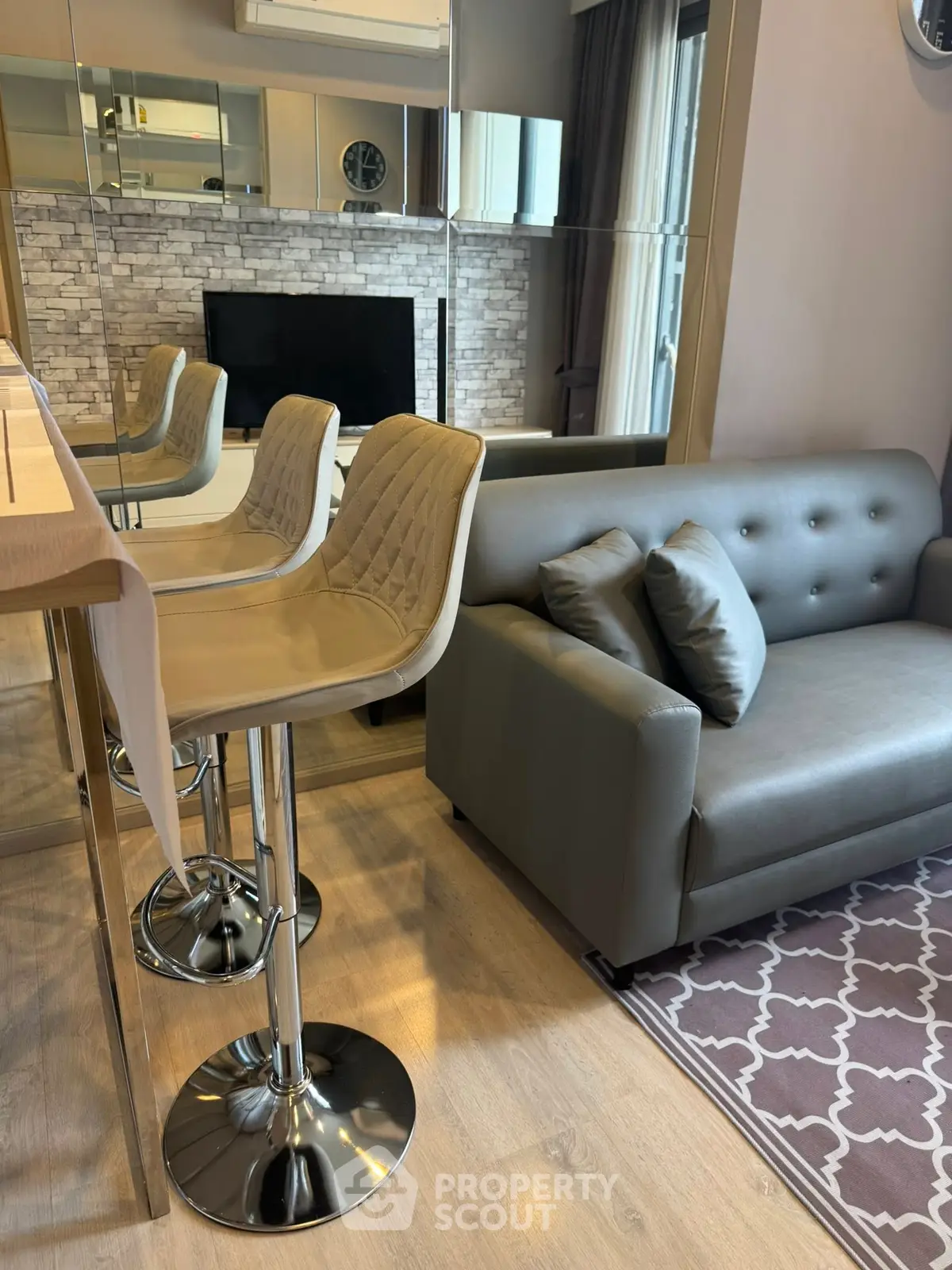 Modern living room with stylish bar stools and cozy sofa, featuring a mirrored wall and elegant decor.