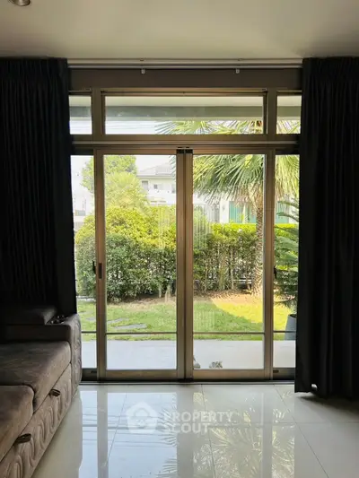 Spacious living room with large glass doors opening to a lush garden view