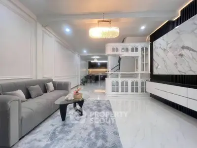 Luxurious living room with elegant chandelier and modern decor, featuring a plush gray sofa and marble accents.