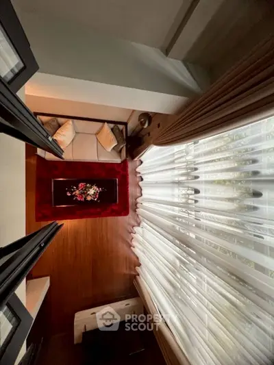 Elegant living room with plush sofa, red rug, and floor-to-ceiling curtains for a cozy ambiance.