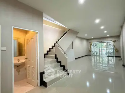 Spacious modern living room with sleek staircase and large windows for natural light.