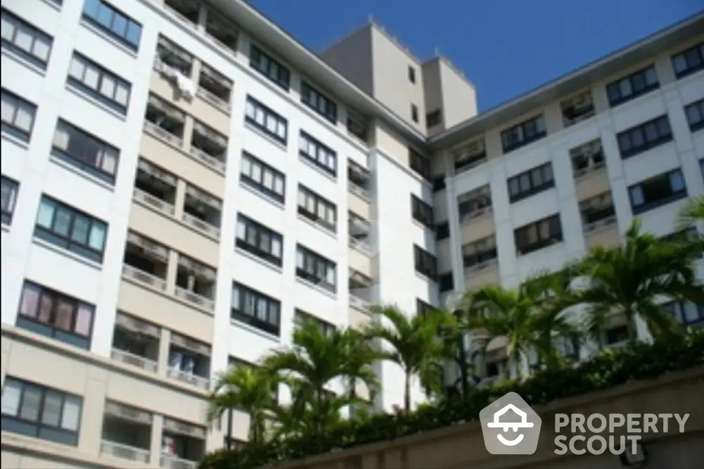 Sunlit modern apartment building with lush greenery, showcasing spacious balconies and a serene urban living environment.