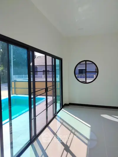 Bright room with large windows overlooking a pool, featuring modern design and ample natural light.