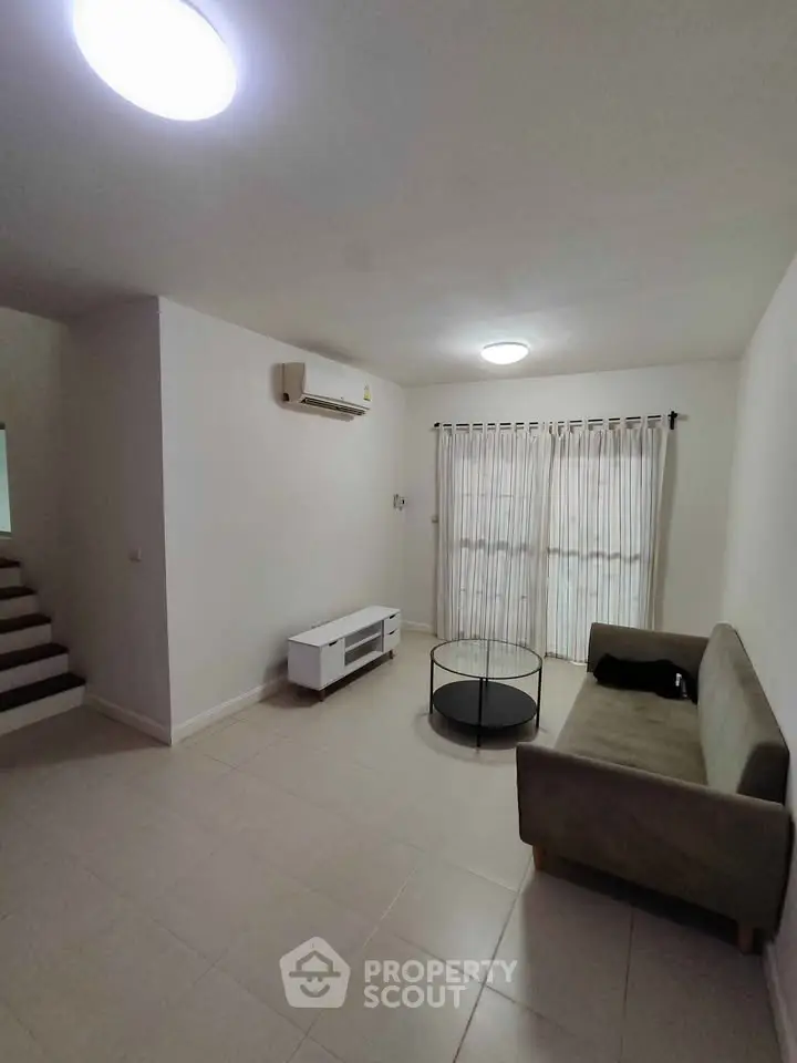 Spacious living room with modern sofa, air conditioning, and natural light from large windows.
