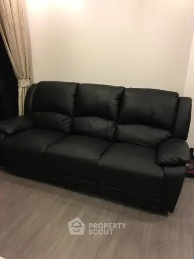 Luxurious black leather sofa in modern living room with elegant curtains and wooden flooring.