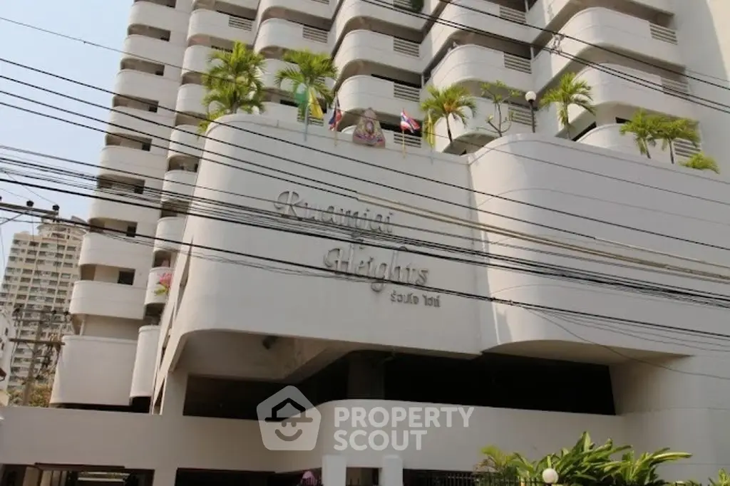 Modern high-rise building exterior with balconies and palm trees, showcasing urban living.