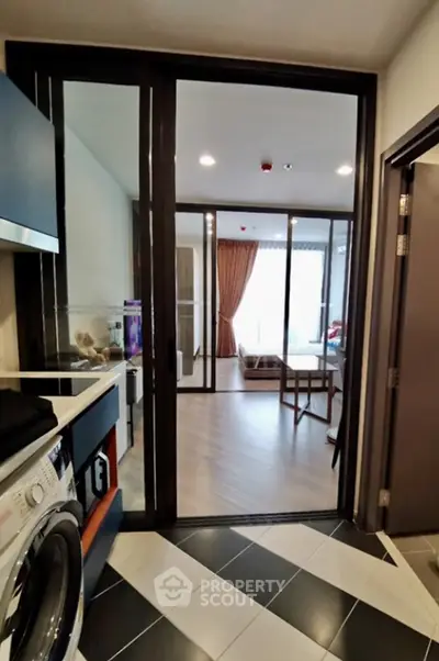 Modern apartment interior with open layout, featuring a washing machine and spacious living area with large windows.