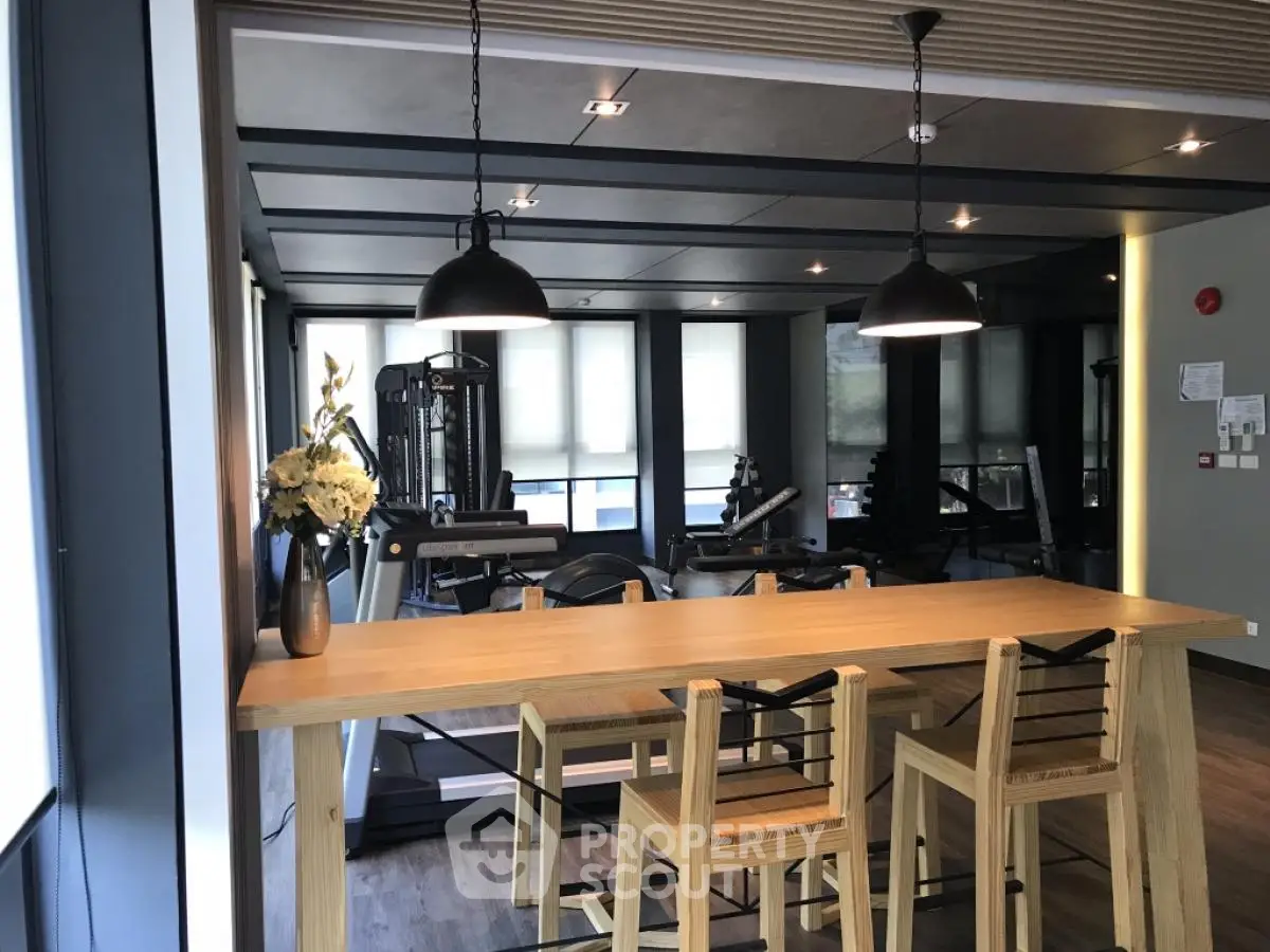 Modern gym with wooden table and chairs, featuring state-of-the-art fitness equipment and stylish lighting.