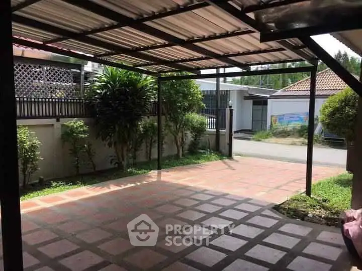 Spacious covered parking area with tiled flooring and garden view in residential property.