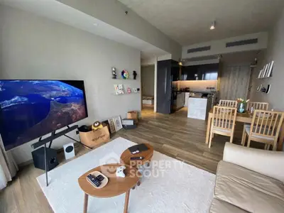 Modern living room with open kitchen, featuring stylish furniture and large TV, perfect for entertainment.